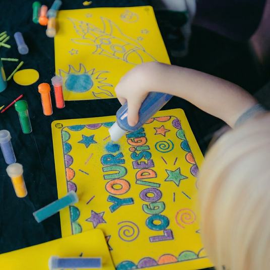 Child coloring on a yellow activity book with markers and crayons.
