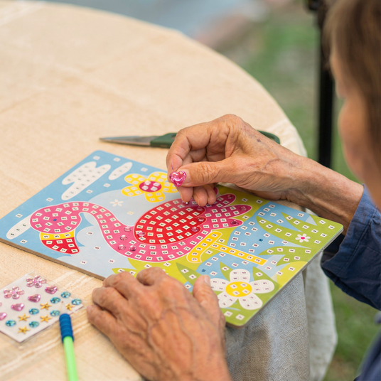 Person working on a craft project with a colorful flamingo design on a wooden board.