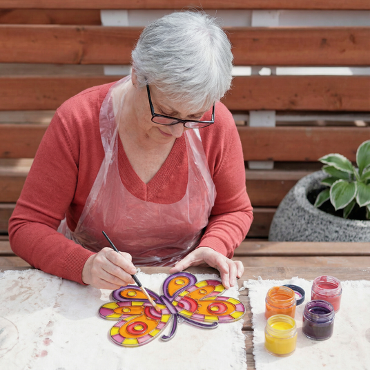Person painting a colorful butterfly on a cake outdoors