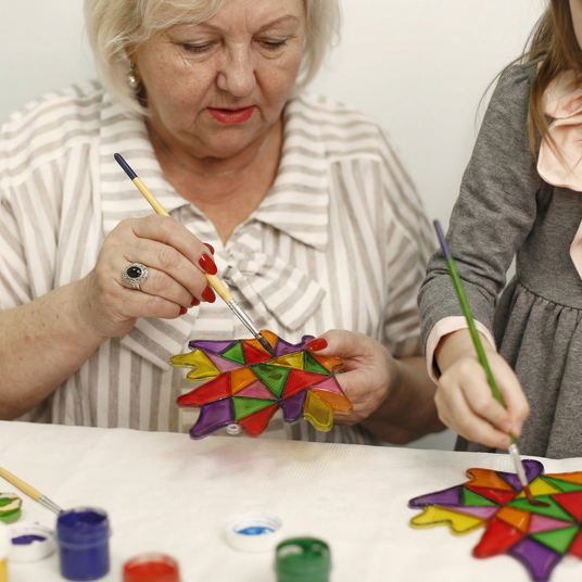 Two women painting colorful star-shaped objects on a table.
