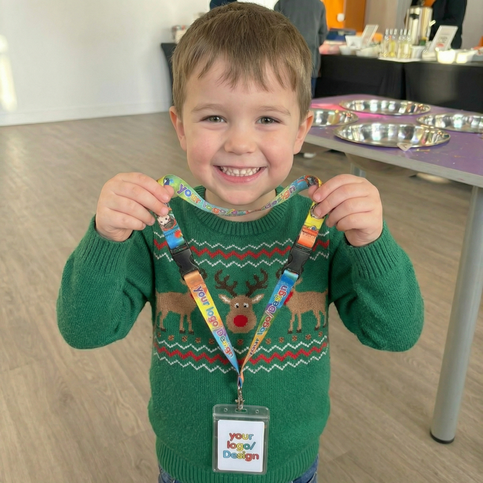 Child wearing a green sweater with reindeer design, holding a colorful lanyard with a name tag.