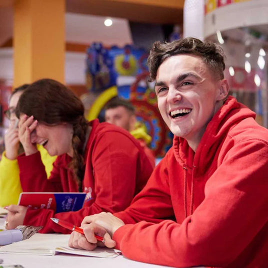 Two people in red hoodies sitting at a table with colorful decorations in the background